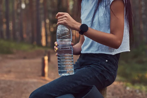 Foto ritagliata di una ragazza hipster turistica tiene una bottiglia d'acqua, fermato a riposare in una bella foresta autunnale . — Foto Stock
