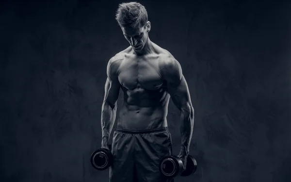 Black and white photo of ectomorph bodybuilder posing with dumbbells and looks down.