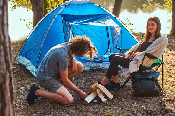 Unga hiker par läger i skogen. Ung kille försöker tända en eld. — Stockfoto