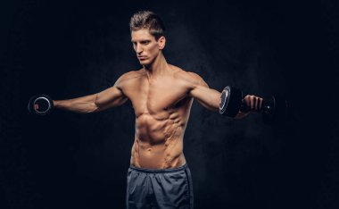 Yakışıklı gömleksiz adam şık saç ve kas ectomorph vücut egzersizleri dumbbells ile yapıyor.