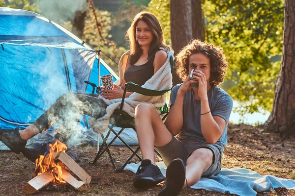 Un par de caminatas en el bosque. Atractiva pareja calentándose cerca de una fogata en el campamento . — Foto de Stock