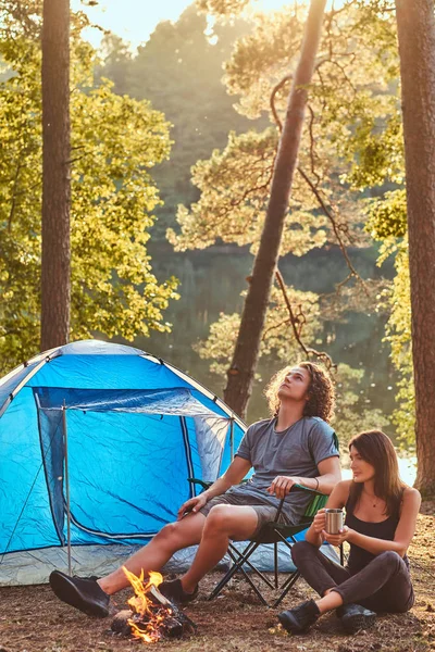 Et ungt par fotturister som sitter ved bålet i skogen på solskinnsdag. . – stockfoto