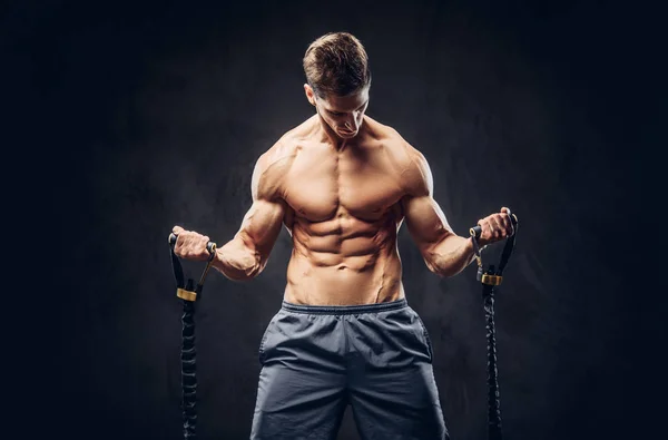 Bonito homem sem camisa com cabelo elegante e ectomorfo muscular fazendo os exercícios com um expansor . — Fotografia de Stock