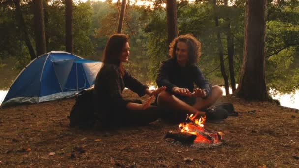 Giovane coppia nella foresta autunnale davanti al fuoco con tenda da campeggio durante il tramonto . — Video Stock