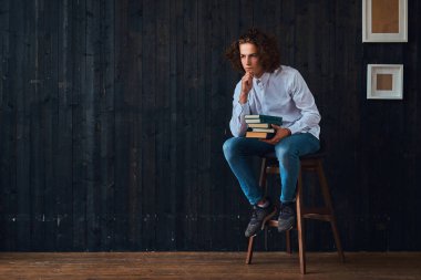 Eğitim sevgisi. Minimalist iç ile bir odada bir sandalyede otururken kitaplar dalgın öğrenci tutar.