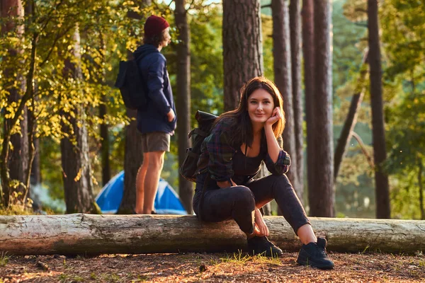 Töprengő turista lány tart kezében az álla ülve egy fa törzse, és tart egy okostelefon, az erdő. — Stock Fotó