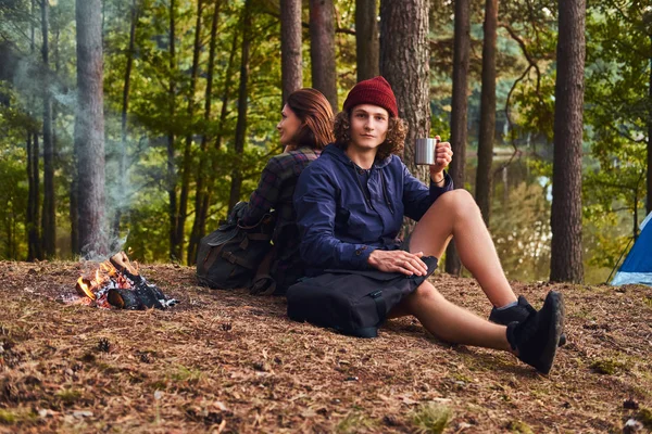 Fiatal turista házaspár ült vissza, vissza, miközben felmelegedés a következő látnivaló közelében: egy tábortűz a tábor az erdő. — Stock Fotó