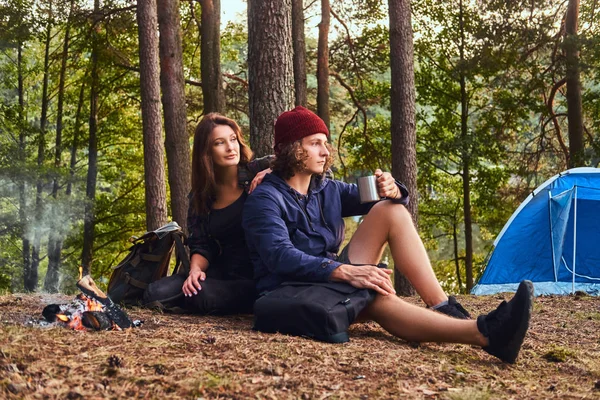 Portret para - przystojny facet kręcone i urocza dziewczyna siedzi razem w lesie. — Zdjęcie stockowe