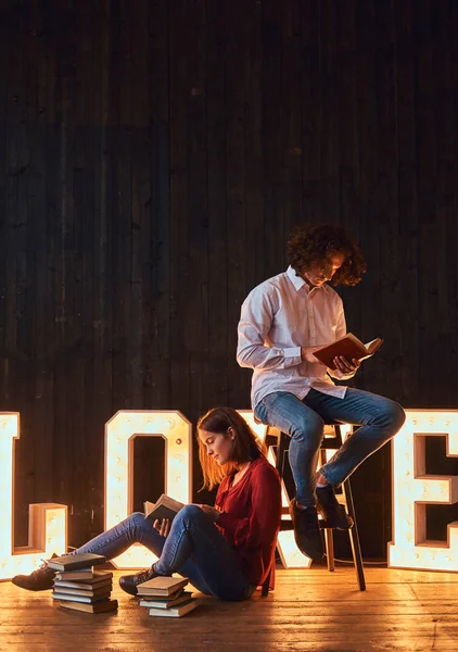 Jovem casal estudante lendo juntos em uma sala decorada com letras volumosas com iluminação . — Fotografia de Stock