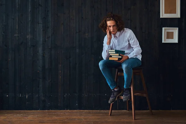 L'amour de l'éducation. Étudiant pensif tient des livres alors qu'il est assis sur une chaise dans une pièce à l'intérieur minimaliste . — Photo