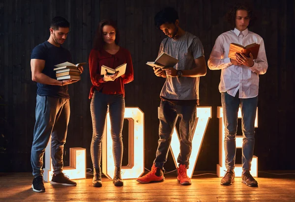 Amor pela educação. Grupo internacional de estudantes com livros em sala decorada com letras volumosas com iluminação . — Fotografia de Stock