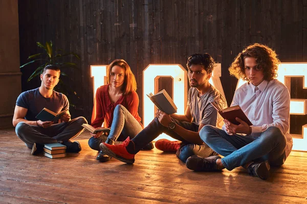 Grupo internacional de estudantes lendo livros em uma sala decorada com letras volumosas com iluminação . — Fotografia de Stock
