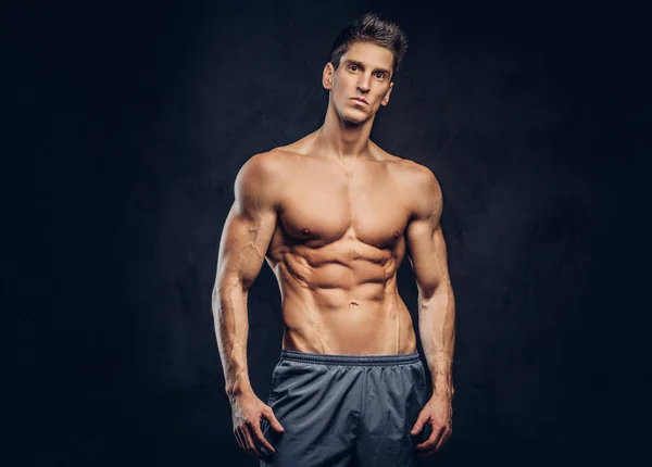 Handsome shirtless ectomorph bodybuilder with stylish hair posing on a dark background. — Stock Photo, Image