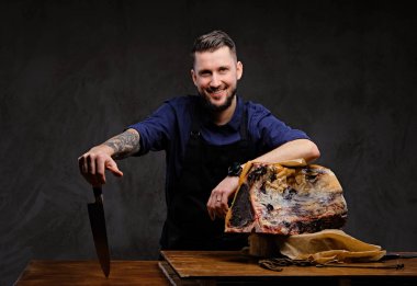 Bir bıçak ve bir tablo ile koyu arka plan üzerinde özel kurutulmuş et yakınındaki poz gülümseyen Şef aşçı tutar.