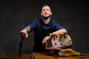 Şef aşçı bıçak ve poz karanlık bir arka plan üzerinde özel kurutulmuş et bir tabloyla yakın tutar.