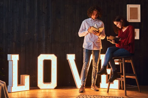 Joven pareja de estudiantes leyendo juntos en una habitación decorada con voluminosas letras con iluminación . — Foto de Stock