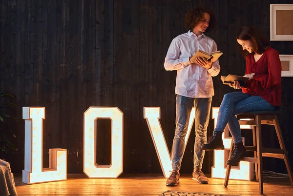 Joven pareja de estudiantes leyendo juntos en una habitación decorada con voluminosas letras con iluminación . — Foto de Stock