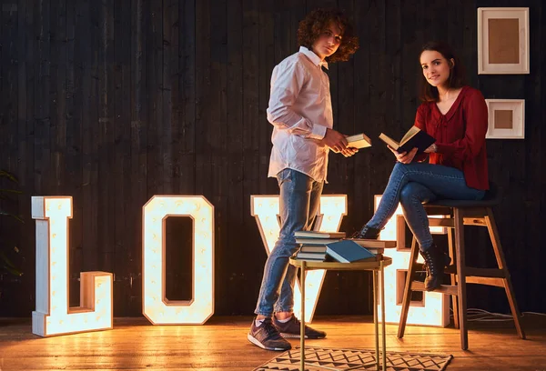 Joven pareja de estudiantes leyendo juntos en una habitación decorada con voluminosas letras con iluminación . — Foto de Stock