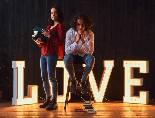 Amor por la educación. Pareja de estudiantes con libros en una habitación decorada con letras voluminosas con iluminación . — Foto de Stock