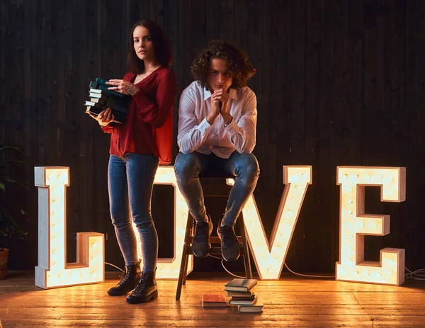 Amor por la educación. Pareja de estudiantes con libros en una habitación decorada con letras voluminosas con iluminación . — Foto de Stock