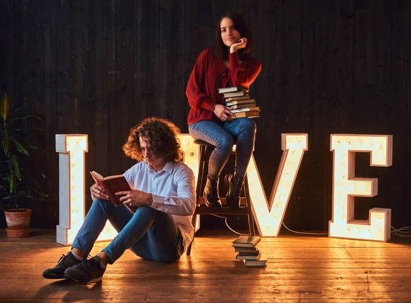 Jeune couple étudiant lisant ensemble dans une salle décorée de lettres volumineuses avec éclairage . — Photo