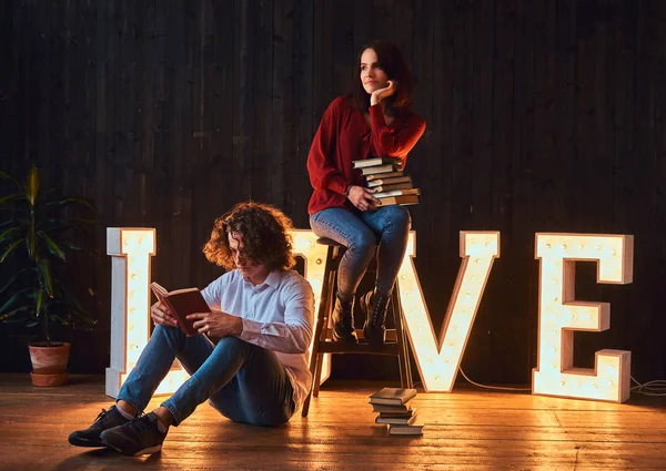 Jeune couple étudiant lisant ensemble dans une salle décorée de lettres volumineuses avec éclairage . — Photo