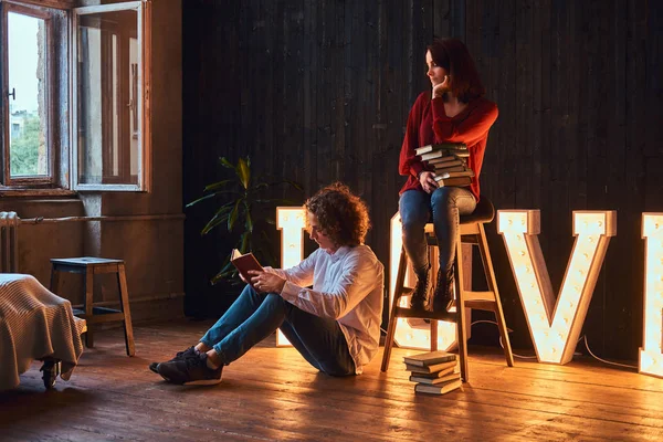 Joven pareja de estudiantes leyendo juntos en una habitación decorada con voluminosas letras con iluminación . — Foto de Stock