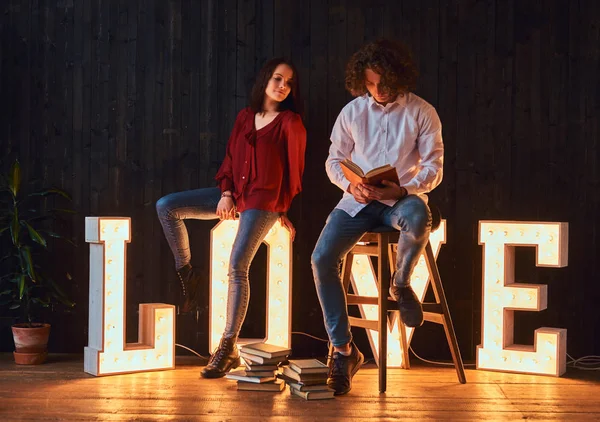 Jeune couple étudiant lisant ensemble dans une salle décorée de lettres volumineuses avec éclairage . — Photo