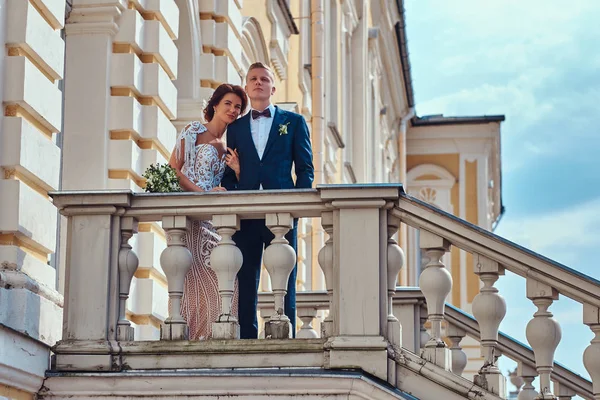 Full body portrait of happy newlyweds embracing while posing on the stairs of the beautiful old palace. — Stock Photo, Image