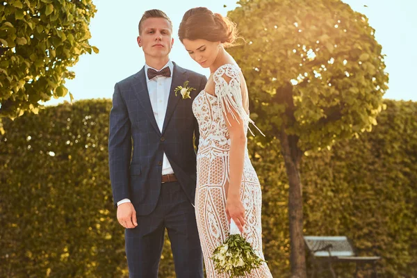 Retrato de belos recém-casados - noiva encantadora abraçar seu belo noivo em um parque . — Fotografia de Stock