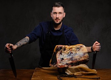 Şef aşçı bıçaklar ve poz koyu arka plan üzerinde özel kurutulmuş et bir tabloyla yakın tutar.