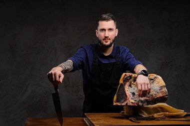 Şef aşçı bıçak ve poz karanlık bir arka plan üzerinde özel kurutulmuş et bir tabloyla yakın tutar.