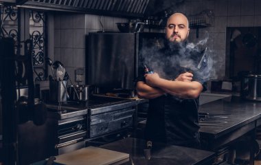 Siyah üniforma duman e-sigara mutfakta dururken sakallı şefi.