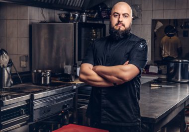 Mutfakta çapraz kolları olan siyah üniforma ayakta acımasız sakallı Şef aşçı.