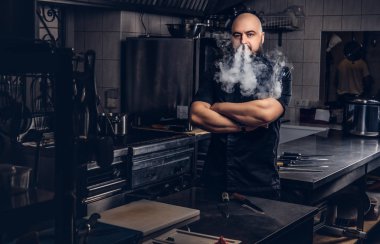 Siyah üniforma duman e-sigara mutfakta dururken sakallı şefi.