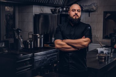 Mutfakta çapraz kolları olan siyah üniforma ayakta acımasız sakallı Şef aşçı.