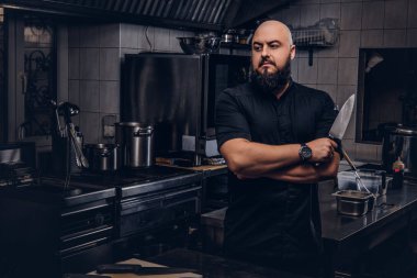 Siyah üniformalı sakallı aşçı bıçak ve Çapraz kollar ile ayakta tutan mutfakta.