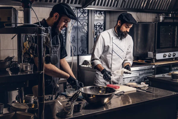 Deux cuisiniers brutaux vêtus d'uniformes préparant des sushis dans une cuisine . — Photo