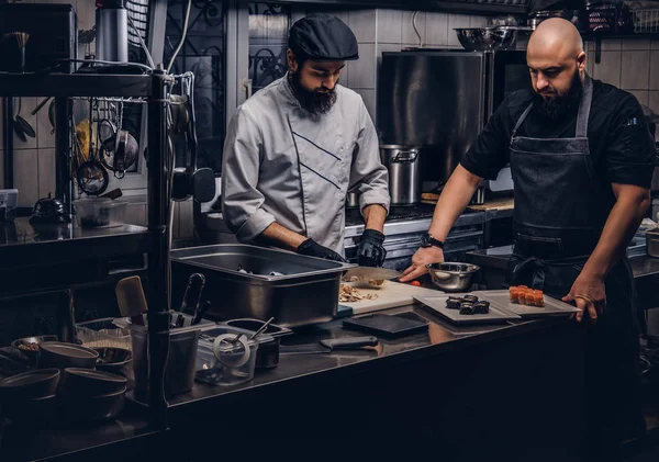 Dos cocineros brutales vestidos con uniformes preparando sushi en una cocina . —  Fotos de Stock