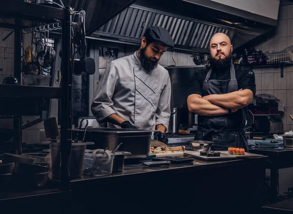 Dos cocineros brutales vestidos con uniformes preparando sushi en una cocina . —  Fotos de Stock