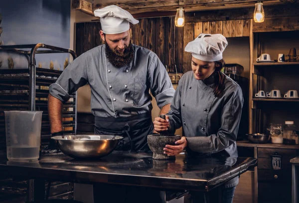 Assistent kok maalt sesamzaadjes in een mortier voor het koken van brood. Chef-kok onderwijs zijn assistent te bakken het brood in de bakkerij. — Stockfoto
