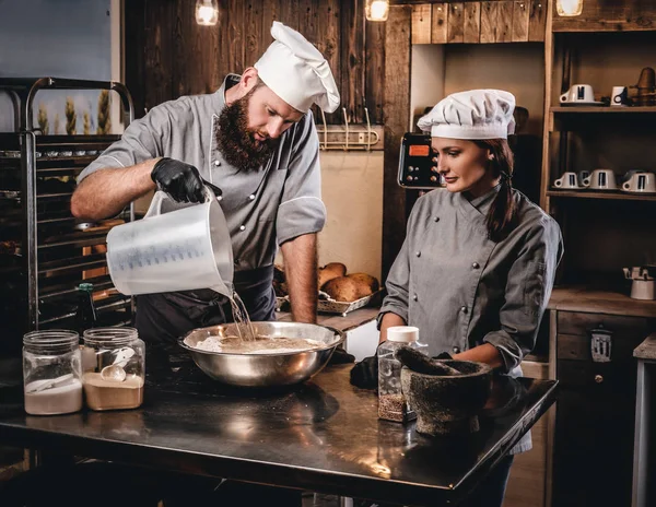 El chef mezcla los ingredientes para la masa. Chef enseñando a su asistente a hornear pan en la panadería . —  Fotos de Stock