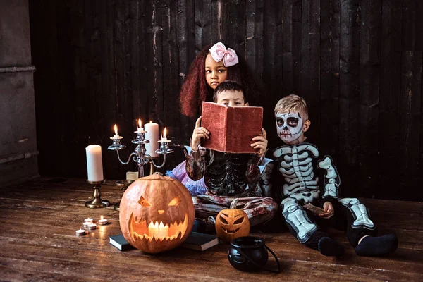 Horror történetek a régi házban, olvasás során Halloween party ijesztő jelmezek-aranyos többnemzetiségű gyerekek csoportja. — Stock Fotó