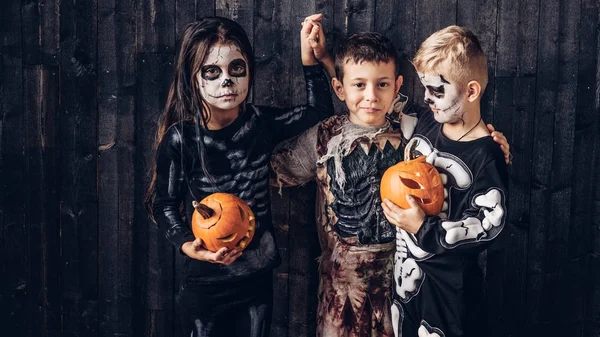 Tres niños multirraciales en trajes de miedo posando con calabazas en una casa vieja . —  Fotos de Stock