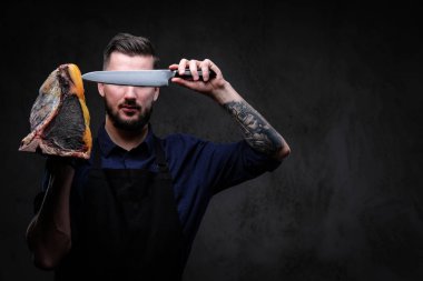 Şef aşçı bıçak ve büyük özel tedavi et parçası karanlık bir arka plan üzerinde tutar.