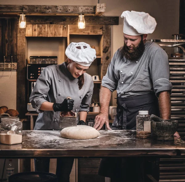 Chef teaching his assistant to bake the bread in a bakery.