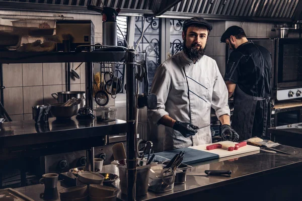 Dois cozinheiros brutais vestidos com uniformes preparando sushi em uma cozinha . — Fotografia de Stock