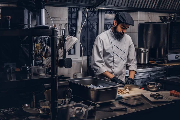 Bärtige Köchin in Uniform und Hut bereitet in der Küche Sushi zu. — Stockfoto