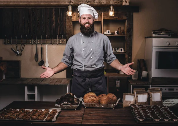 Promotion in bakery. Handsome bearded chef in uniform showing fresh bread in the kitchen. Welcome in bakery.