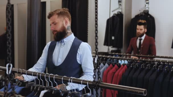 Homem elegante barbudo em terno elegante escolhe roupas no salão de alfaiate . — Vídeo de Stock
